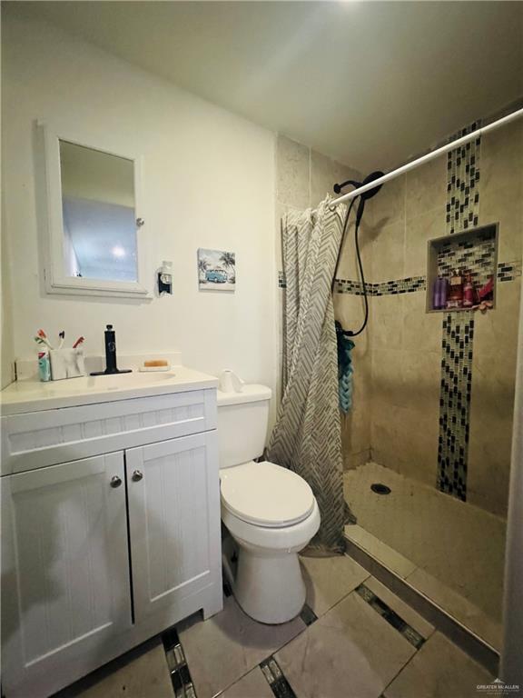 full bath featuring toilet, a tile shower, and vanity