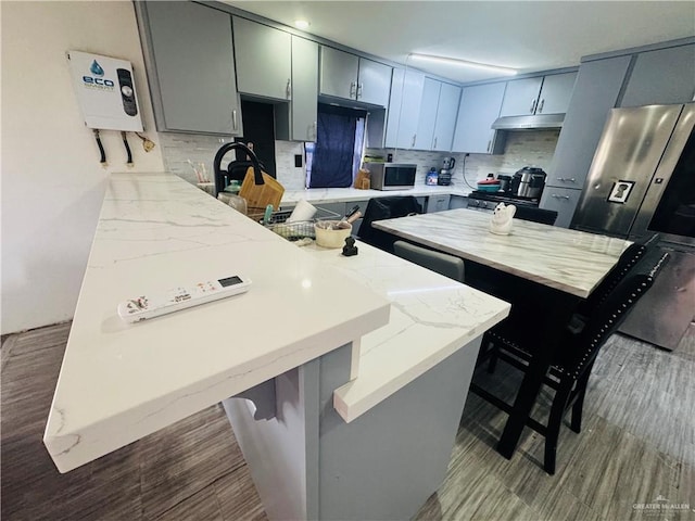 kitchen with a breakfast bar area, tasteful backsplash, appliances with stainless steel finishes, a kitchen island, and a peninsula