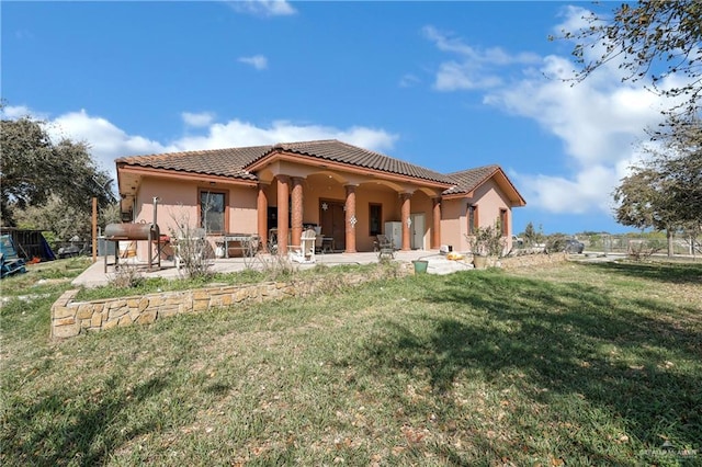 back of property with stucco siding, a yard, a patio area, and a tiled roof