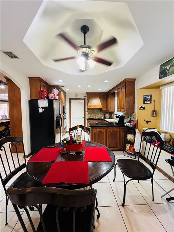 dining room with visible vents, light tile patterned floors, arched walkways, a raised ceiling, and a ceiling fan