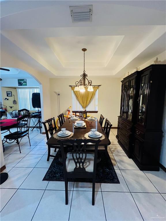 dining area with light tile patterned floors, visible vents, a raised ceiling, and an inviting chandelier