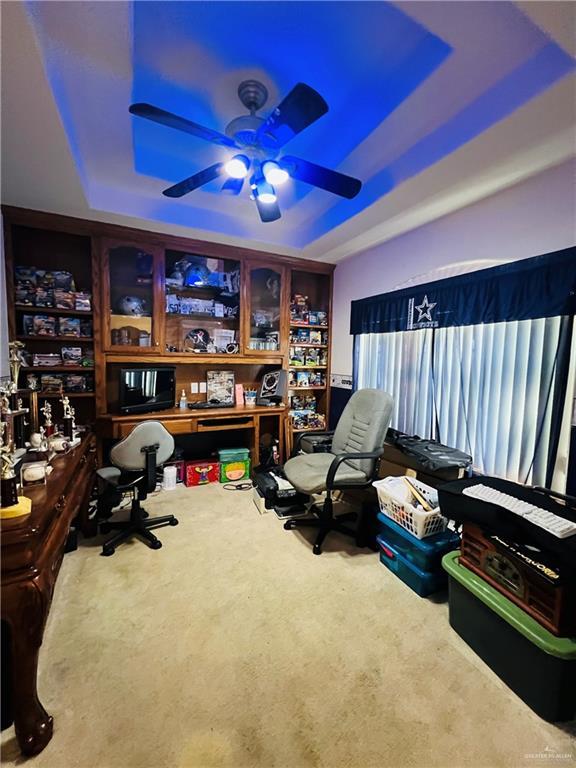 home office featuring a tray ceiling, carpet floors, and a ceiling fan