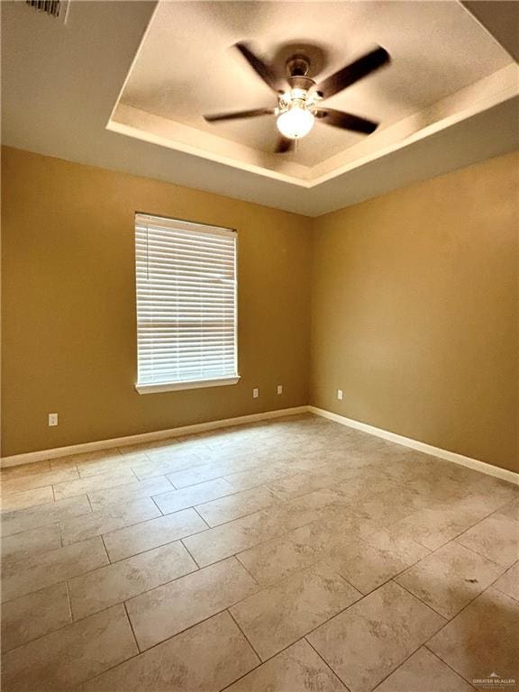 empty room with ceiling fan and a tray ceiling