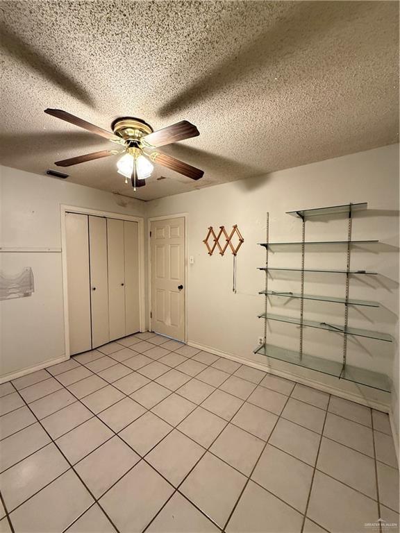 interior space with a textured ceiling, light tile patterned flooring, a ceiling fan, and visible vents