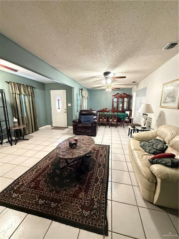 living room featuring visible vents, tile patterned floors, a ceiling fan, and a textured ceiling