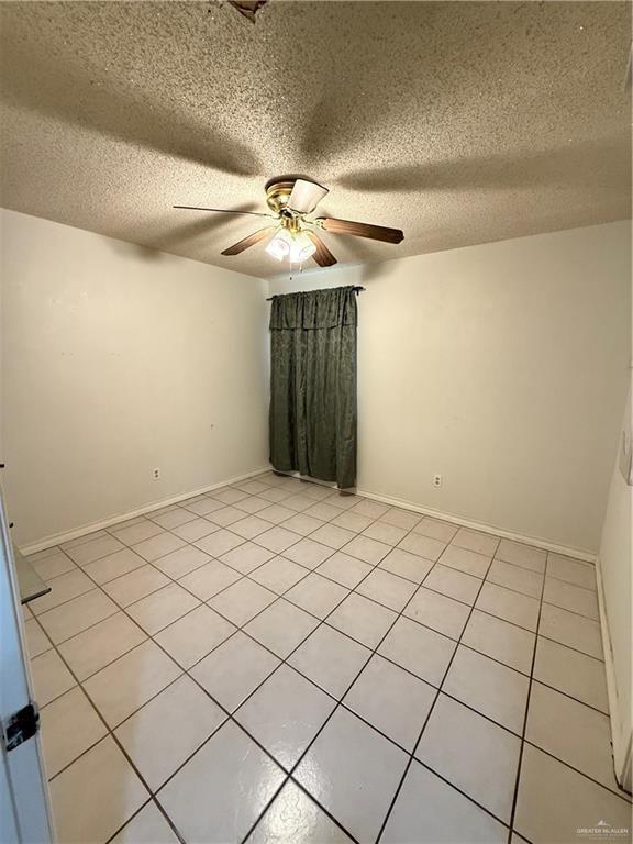 empty room featuring a textured ceiling, ceiling fan, and baseboards