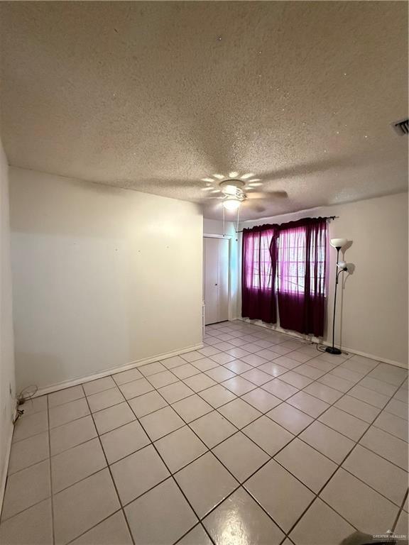 unfurnished room with baseboards, a textured ceiling, light tile patterned flooring, visible vents, and ceiling fan