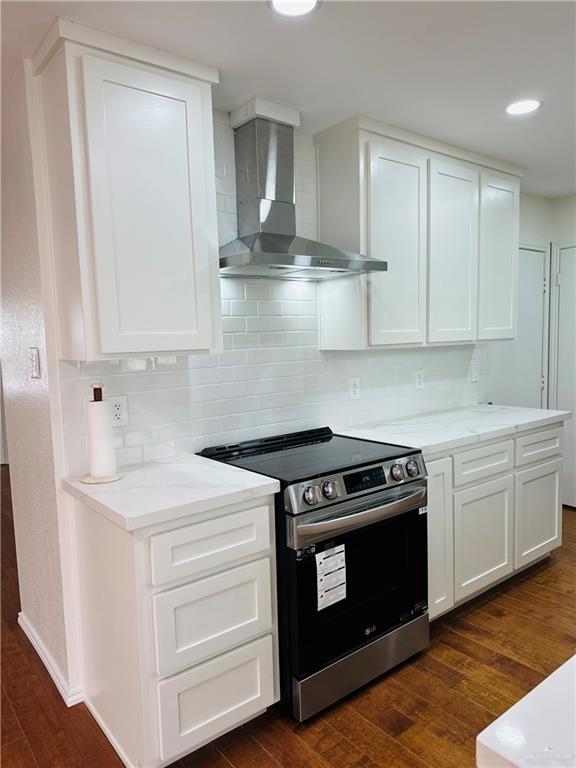 1523 Evergreen Ave, Mission, TX 78572 - kitchen with stainless steel range with electric stovetop, wall chimney range hood, white cabinets, dark wood-type flooring, and backsplash