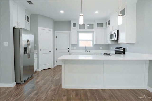 kitchen with glass insert cabinets, a peninsula, stainless steel appliances, pendant lighting, and a sink