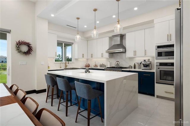 kitchen with tasteful backsplash, wall chimney range hood, pendant lighting, white cabinets, and a kitchen island