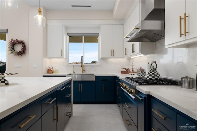 kitchen featuring white cabinets, sink, hanging light fixtures, wall chimney exhaust hood, and blue cabinetry