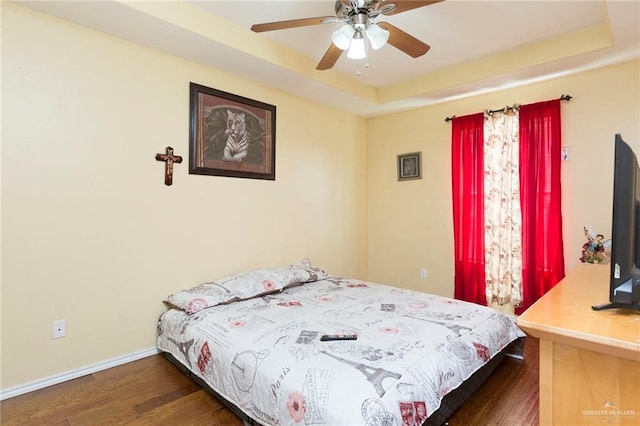 bedroom featuring dark hardwood / wood-style floors, ceiling fan, and a raised ceiling