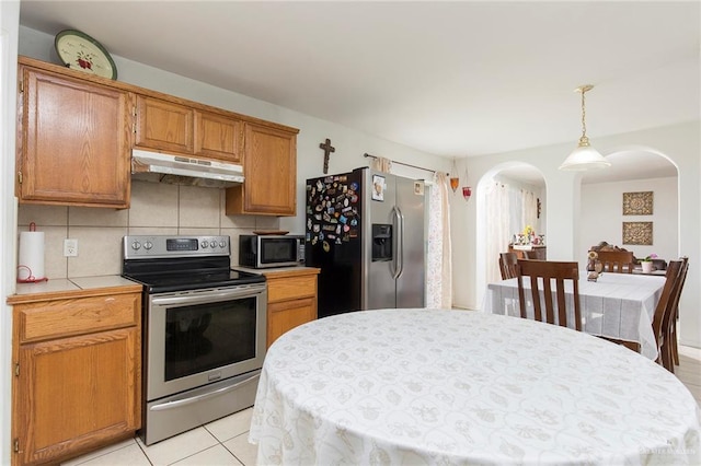 kitchen featuring tile counters, stainless steel appliances, backsplash, pendant lighting, and light tile patterned flooring