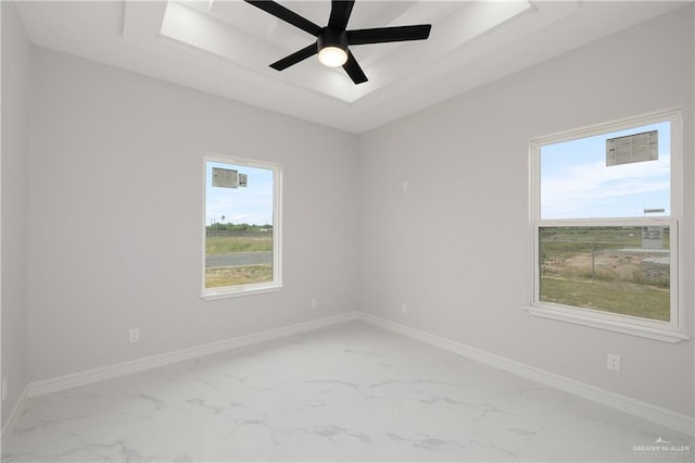spare room featuring marble finish floor, a wealth of natural light, a tray ceiling, and baseboards