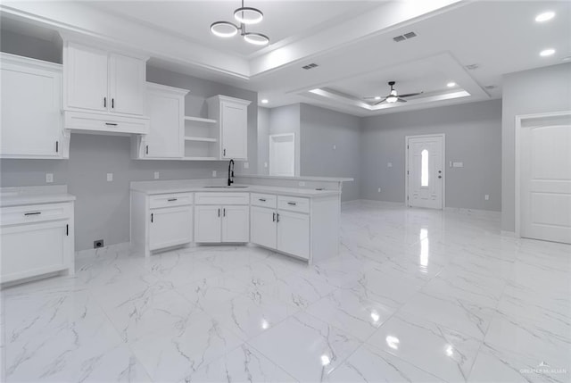 kitchen featuring sink, a raised ceiling, kitchen peninsula, white cabinets, and ceiling fan with notable chandelier