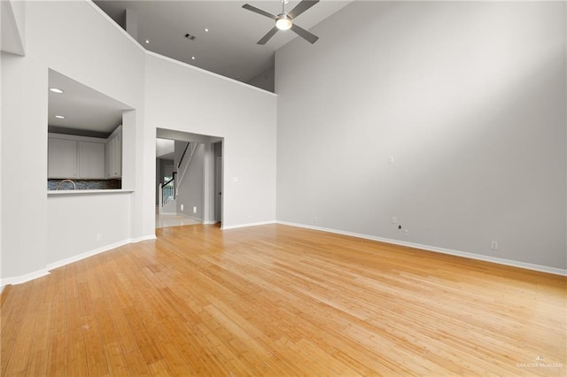 unfurnished living room with ceiling fan, light hardwood / wood-style floors, and a towering ceiling