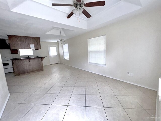 unfurnished living room with ceiling fan with notable chandelier, a raised ceiling, and light tile patterned flooring