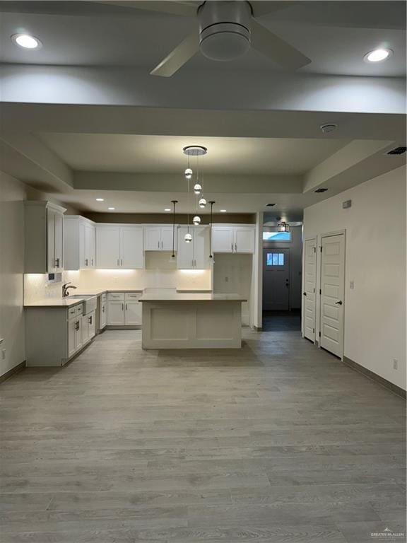 kitchen featuring decorative light fixtures, light wood-type flooring, white cabinetry, and sink