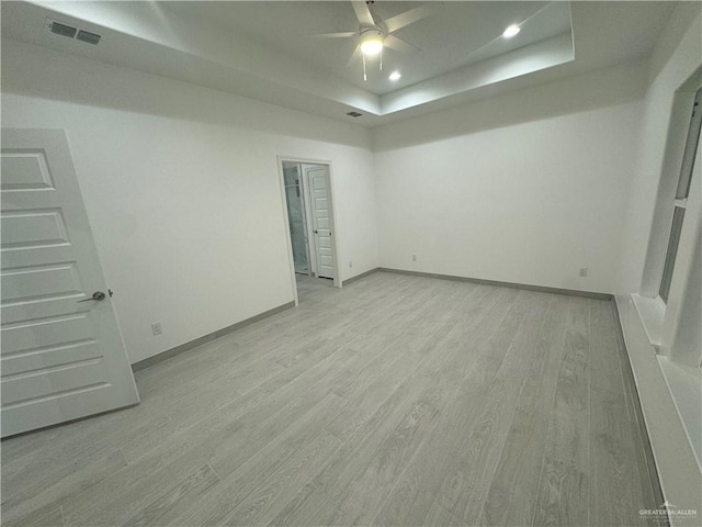 spare room with a tray ceiling, ceiling fan, and light hardwood / wood-style floors