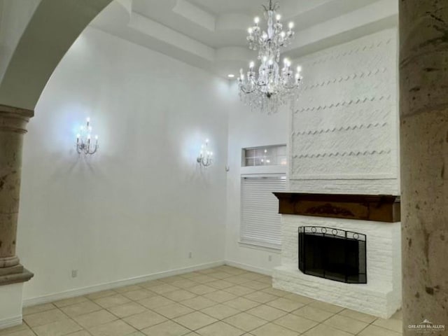 unfurnished living room with a raised ceiling, a stone fireplace, a notable chandelier, a towering ceiling, and light tile patterned flooring