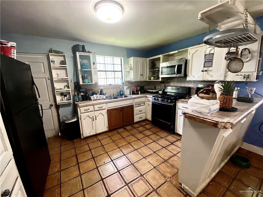 kitchen with tile counters, open shelves, white cabinets, black appliances, and a sink