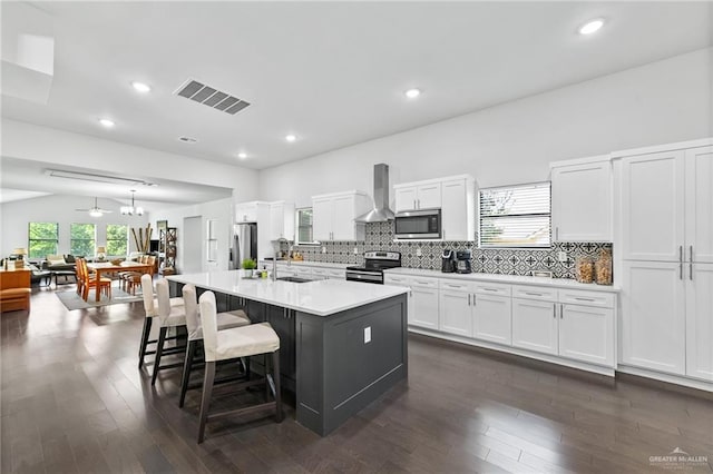 136 W Evergreen St, Boerne, TX 78006 - kitchen featuring stainless steel appliances, wall chimney range hood, a breakfast bar area, white cabinetry, and light countertops