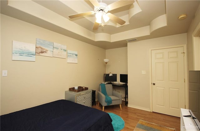 bedroom featuring ceiling fan, light hardwood / wood-style floors, and a raised ceiling