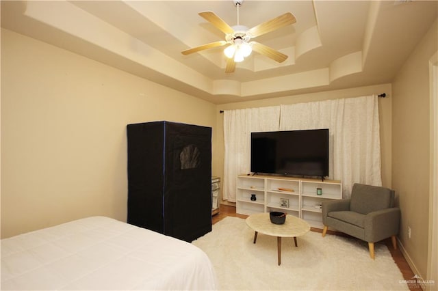 bedroom featuring hardwood / wood-style floors, a raised ceiling, and ceiling fan