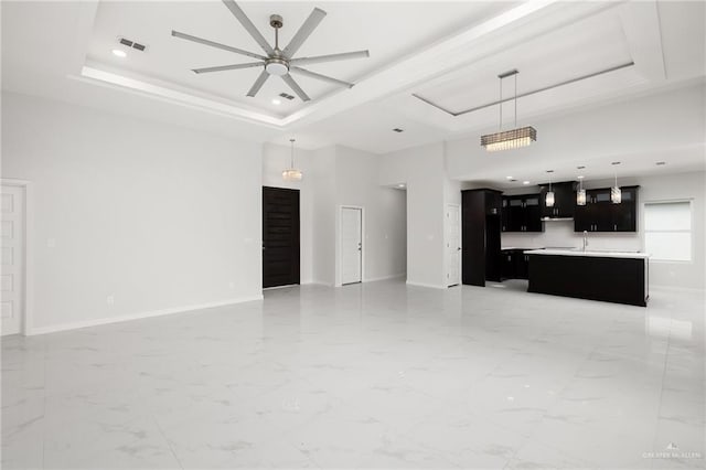 unfurnished living room featuring a raised ceiling, ceiling fan, and sink