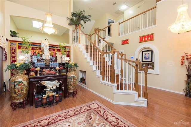 stairway with hardwood / wood-style floors, high vaulted ceiling, and a chandelier