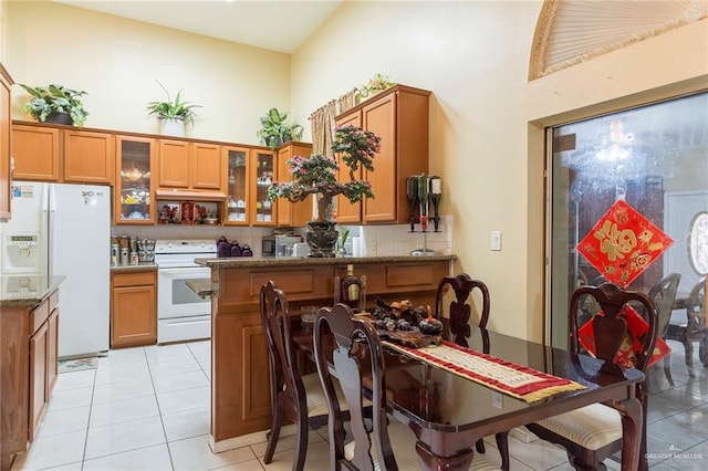 kitchen with decorative backsplash, a kitchen breakfast bar, light stone counters, white appliances, and light tile patterned floors