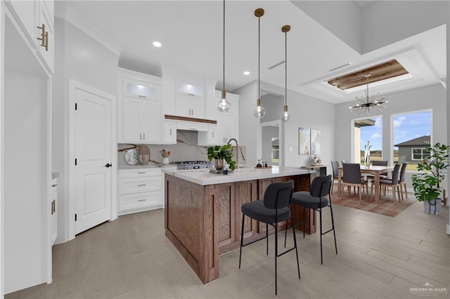 1101 Magnolia St, Mission, TX 78573 - kitchen with an island with sink, glass insert cabinets, white cabinetry, hanging light fixtures, and light wood finished floors