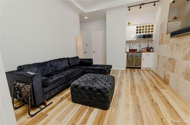 living room featuring track lighting, beverage cooler, bar, and light hardwood / wood-style flooring