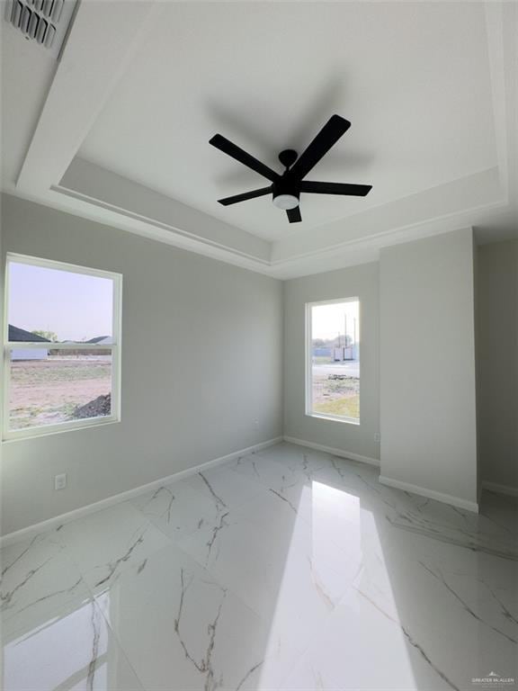 empty room featuring a tray ceiling, baseboards, marble finish floor, and visible vents