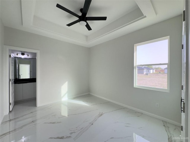 empty room with a tray ceiling, a ceiling fan, baseboards, and marble finish floor