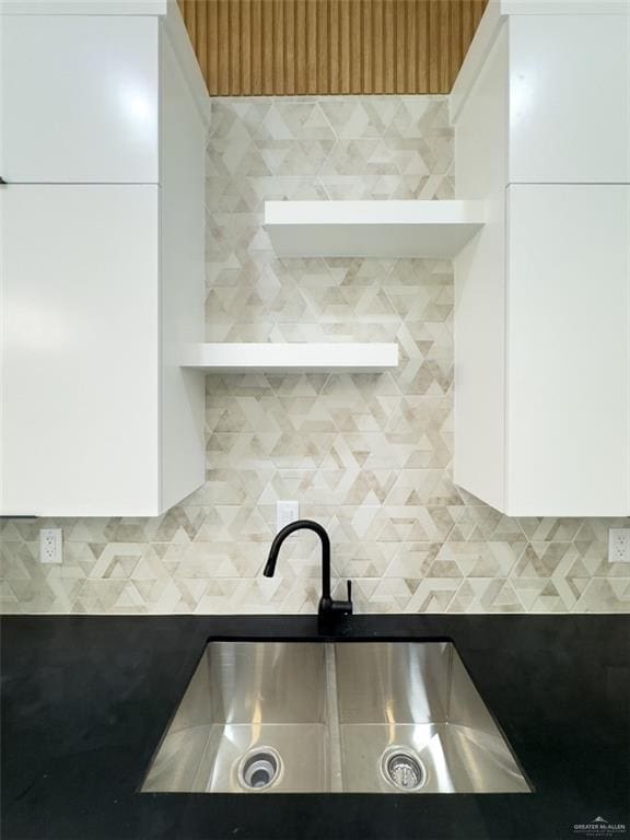 kitchen with dark countertops, white cabinets, tasteful backsplash, and a sink