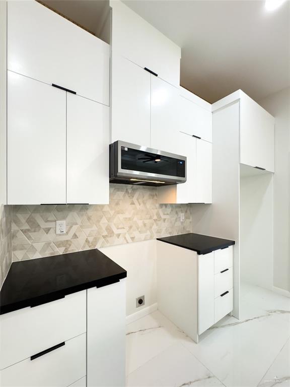 kitchen with stainless steel microwave, marble finish floor, and white cabinetry