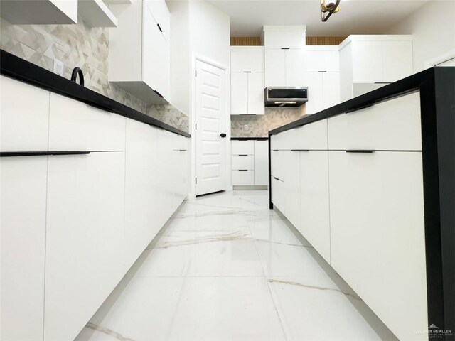 kitchen featuring modern cabinets, marble finish floor, dark countertops, backsplash, and white cabinetry