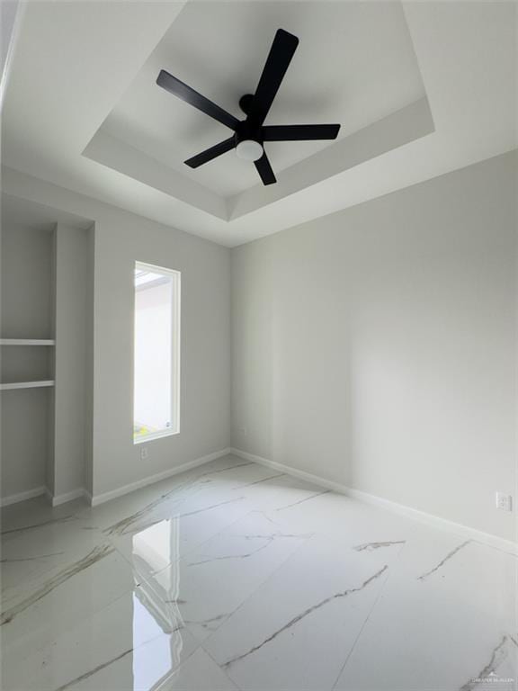 spare room with a tray ceiling, baseboards, marble finish floor, and a ceiling fan