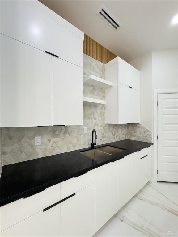 kitchen featuring dark countertops, visible vents, open shelves, marble finish floor, and a sink