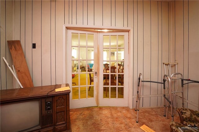 doorway to outside with wooden walls, french doors, and carpet