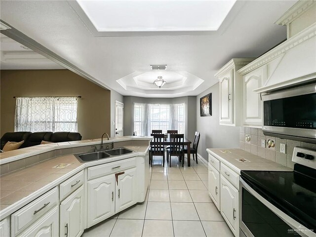 700 Via Cantera Dr, San Juan, TX 78589 - kitchen with stainless steel appliances, a sink, tile counters, a tray ceiling, and white cabinets