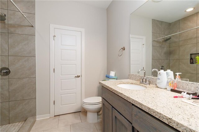 bathroom with tiled shower, tile patterned flooring, vanity, and toilet