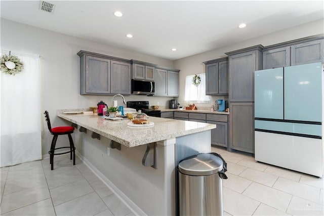 kitchen featuring freestanding refrigerator, stainless steel microwave, electric range, a peninsula, and a breakfast bar