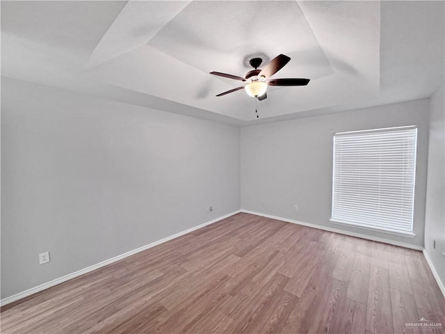 spare room featuring ceiling fan, a raised ceiling, and light wood-type flooring