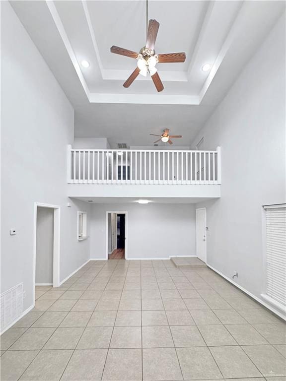 unfurnished living room with a high ceiling, light tile patterned flooring, ceiling fan, and a tray ceiling