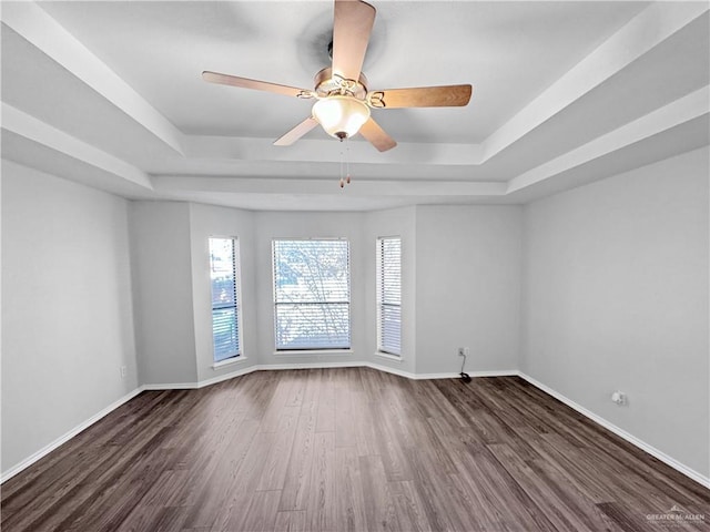 spare room with a tray ceiling, dark wood-type flooring, and ceiling fan