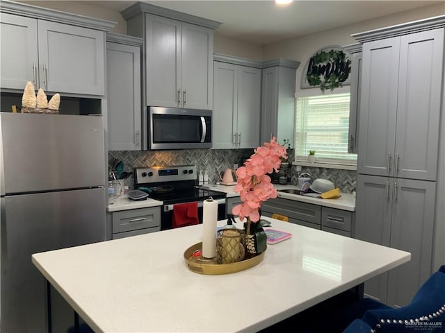 kitchen featuring stainless steel appliances, a breakfast bar, gray cabinetry, and backsplash