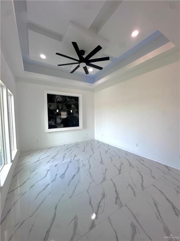 empty room with ceiling fan and a tray ceiling