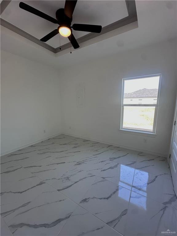 empty room with ceiling fan and a tray ceiling